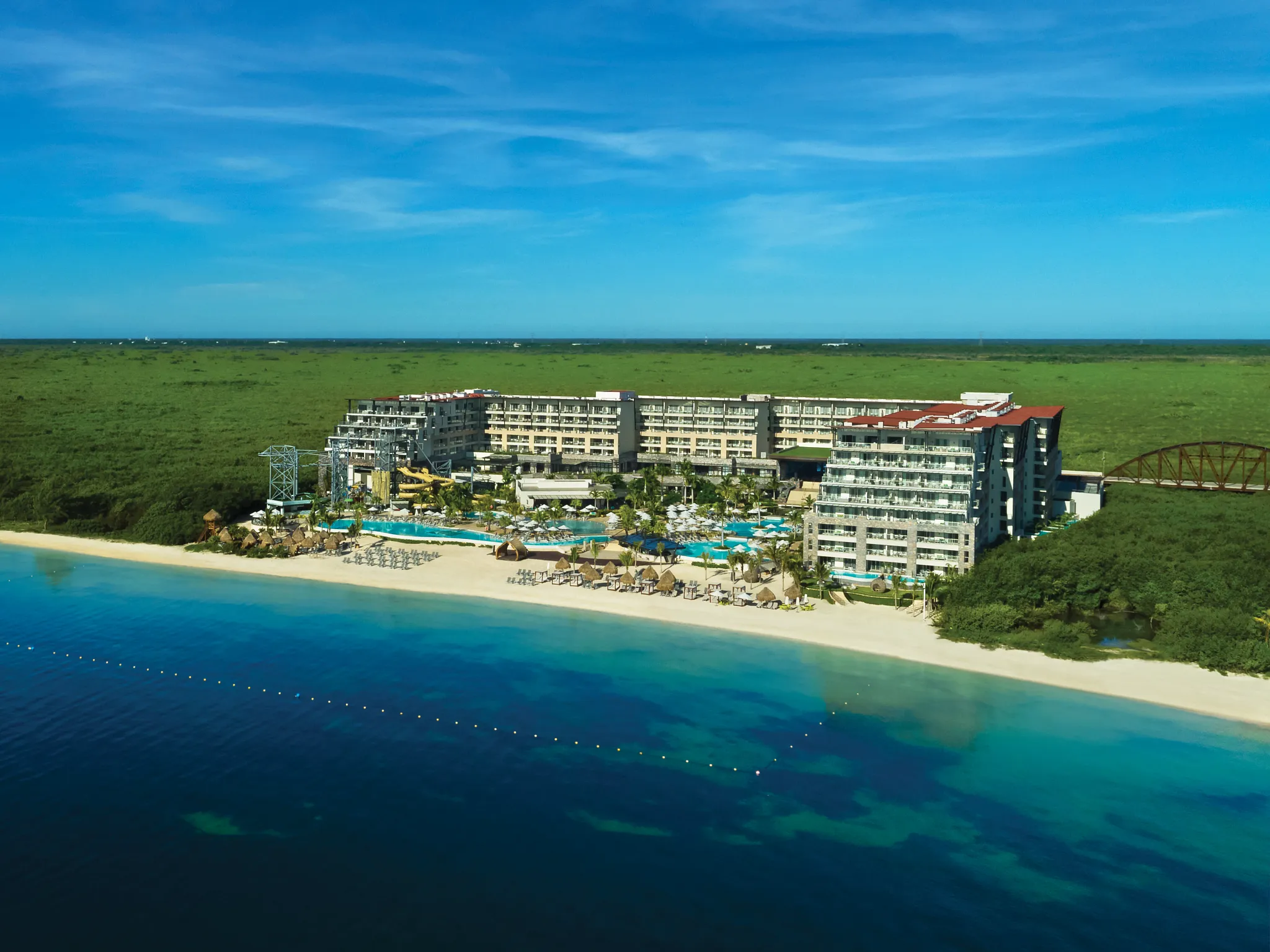 Aerial view of Dreams Natura Resort & Spa beachfront property with pools, beach, and surrounding lush greenery in Riviera Cancun.