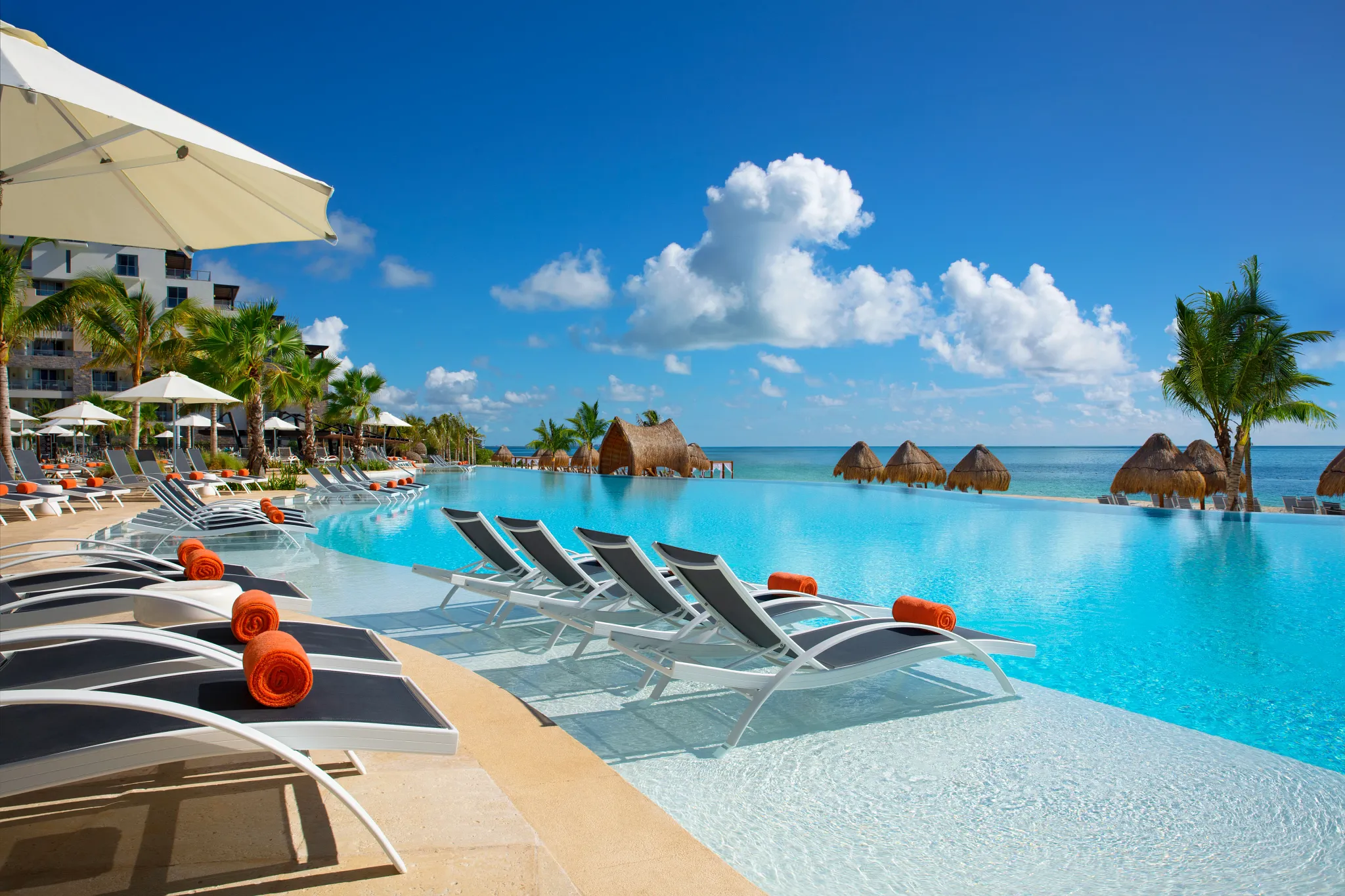 Oceanfront infinity pool with loungers and umbrellas at Dreams Natura Resort & Spa, overlooking the Caribbean Sea in Riviera Cancun.