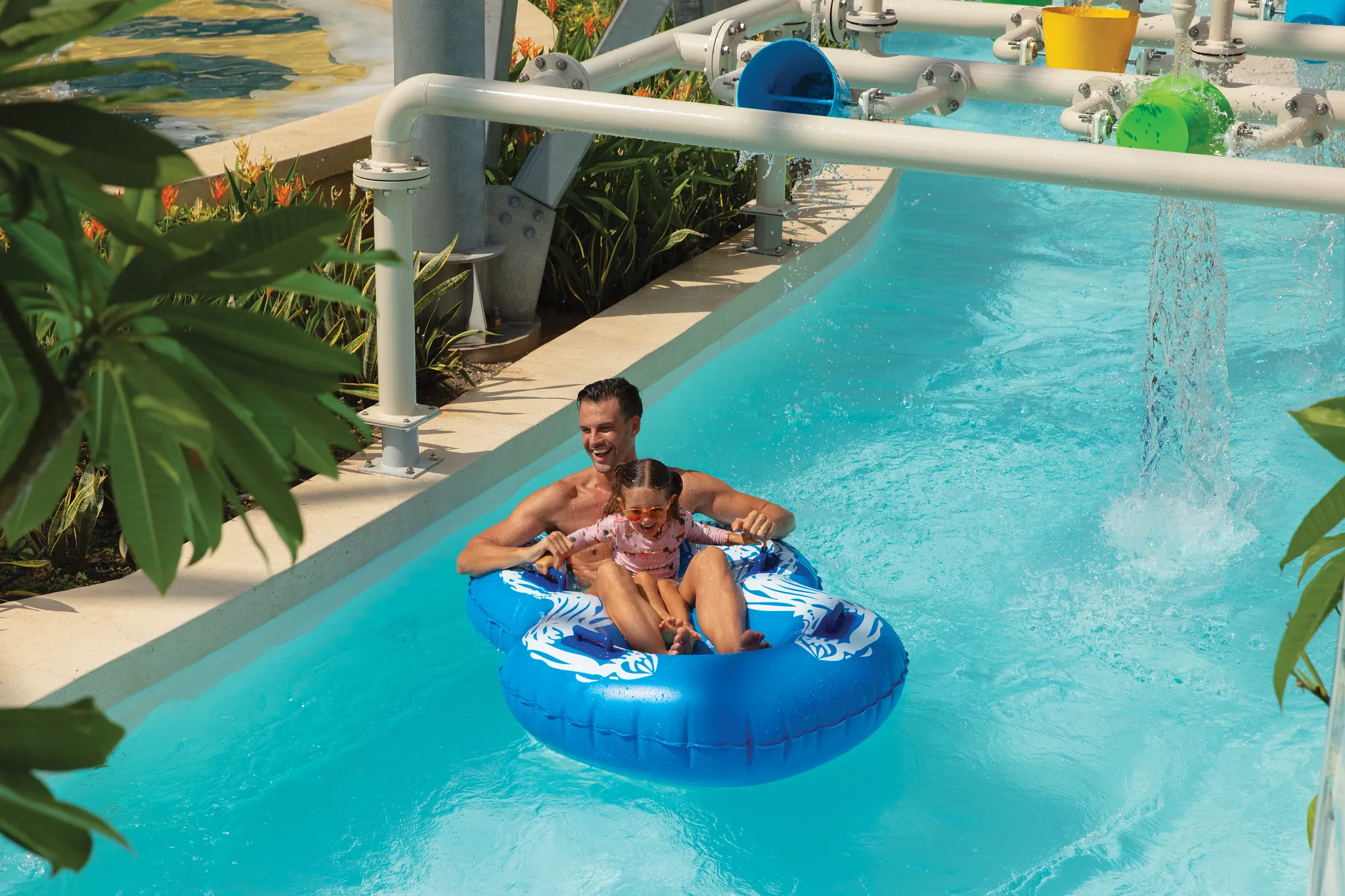 Father and daughter enjoying a lazy river ride on a float at Dreams Natura Resort & Spa water park.