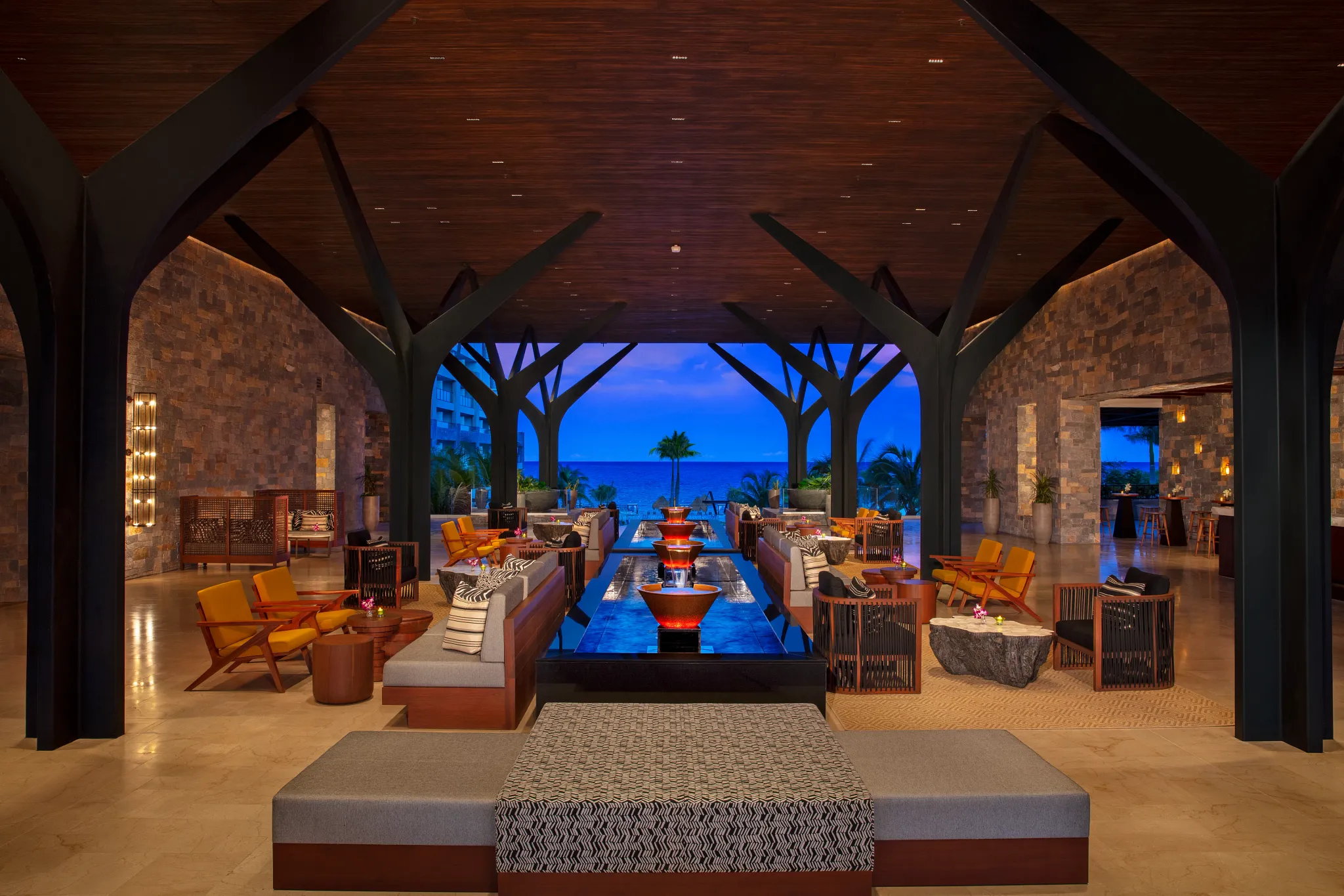 Open-air lobby with modern seating, water feature, and ocean views at sunset at Dreams Natura Resort & Spa.