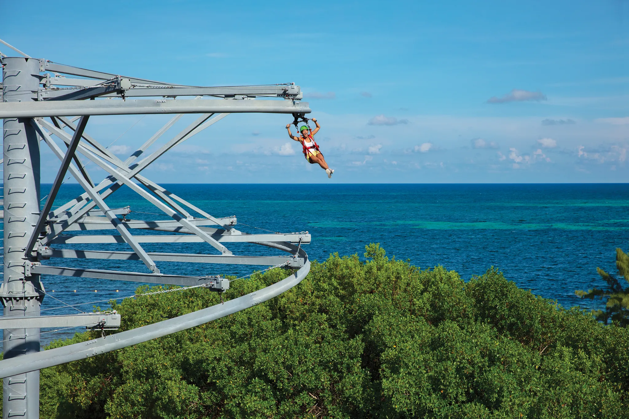 Guest riding a rollglider zipline above lush greenery and ocean views at Dreams Natura Resort & Spa.